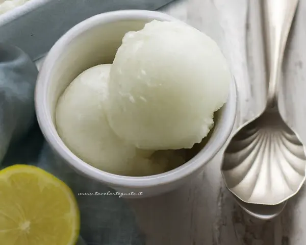 Coppetta di sorbetto al limone, fresca e dissetante, con limone fresco e cucchiaio decorato.