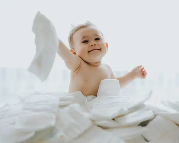 Uśmiechnięty bobas otoczony stertą pieluch. Zastanawiasz się, jakie pieluchy dla noworodka będą najlepsze?