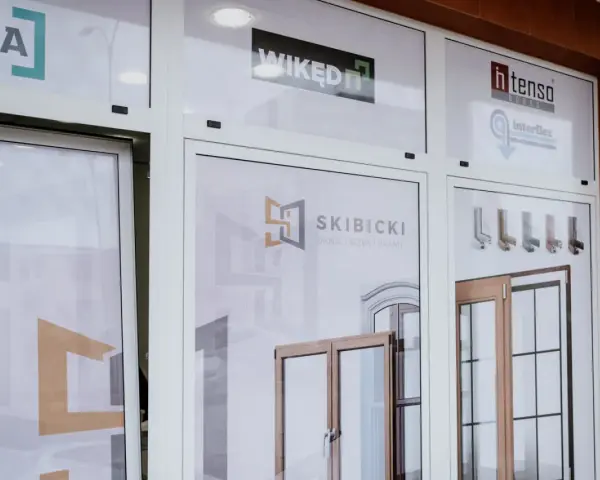 Witryna salonu okien i drzwi z logotypami firm i zdjęciami produktów.