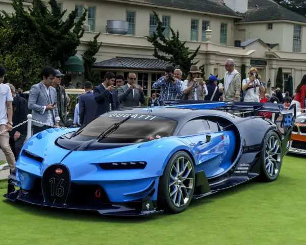 Niebieski Bugatti Veyron z numerem 16 na masce, otoczony tłumem ludzi robiących zdjęcia, na tle eleganckiego budynku.