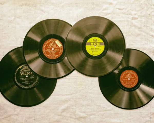 Vier alte Schallplatten liegen auf einer Leinwand. Eine davon hat ein gelbes MGM-Label, die anderen sind von Victrola und Victor. Sie erinnern an die Anfänge des Rocken Roll.