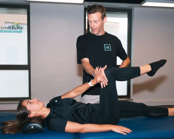 Un kinésithérapeute guide une patiente dans un exercice pour soulager la cruralgie. Elle est allongée sur une table de massage, une jambe pliée, l'autre tendue.