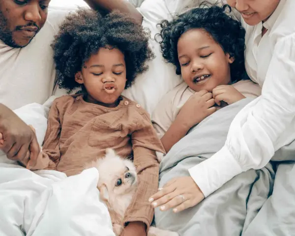 Familie kuschelt im Bett, um sich mit Kindern zu entspannen. Ein kleiner Hund liegt zwischen ihnen.