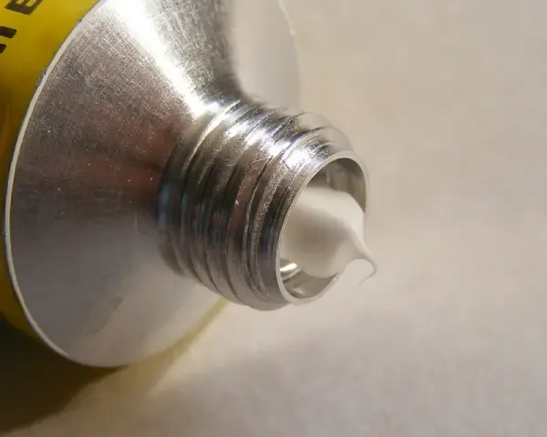 Tubo di alluminio con crema bianca che fuoriesce, mostrando diversi tipi di silicone.