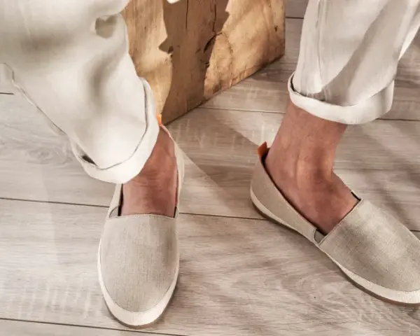 Un uomo indossa espadrillas in tela beige con pantaloni chiari arrotolati. Perfette per un look casual estivo, scopri come abbinarle.