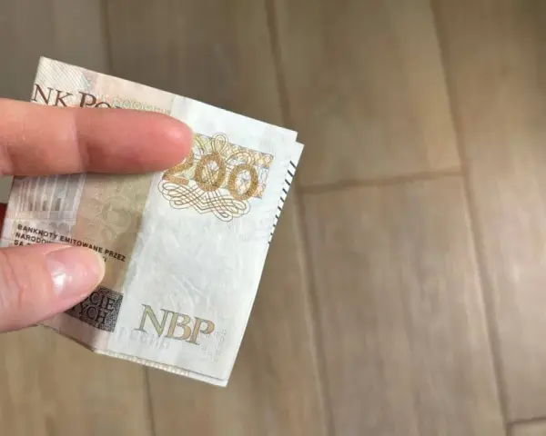 Dłoń trzyma banknot 200 zł. Gdzie można trzymać pieniądze? Familiada podpowie!