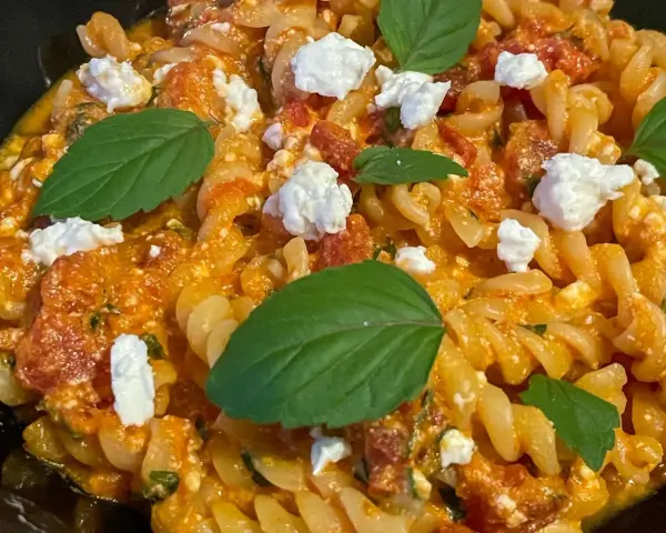 Makaron fusilli w pomarańczowym sosie z kawałkami sera i listkami bazylii.