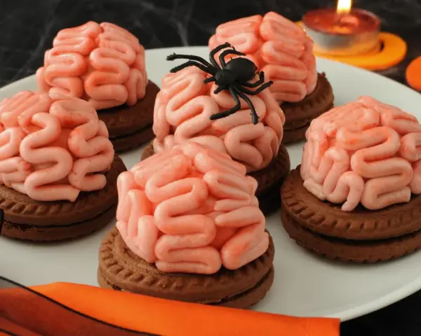 Gruselige Halloween-Nachspeise: Kekse mit Gehirn-förmiger rosa Glasur, dekoriert mit einer Spinne. Kerzen leuchten im Hintergrund.