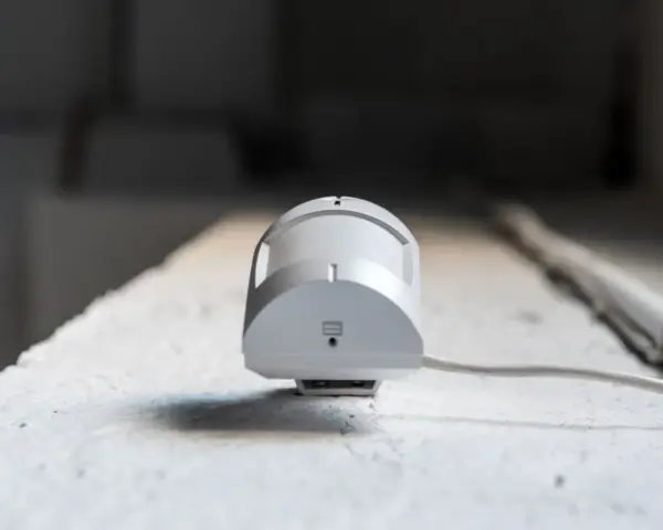 Detector de presencia y movimiento blanco, con cable, montado en superficie rugosa.