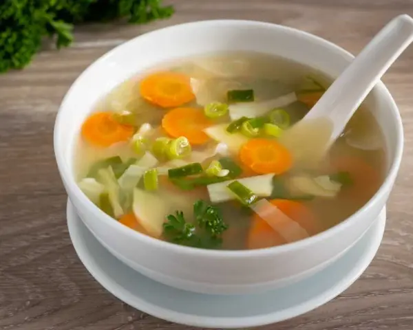 Tazón de sopa de verduras con zanahorias, puerros y perejil.