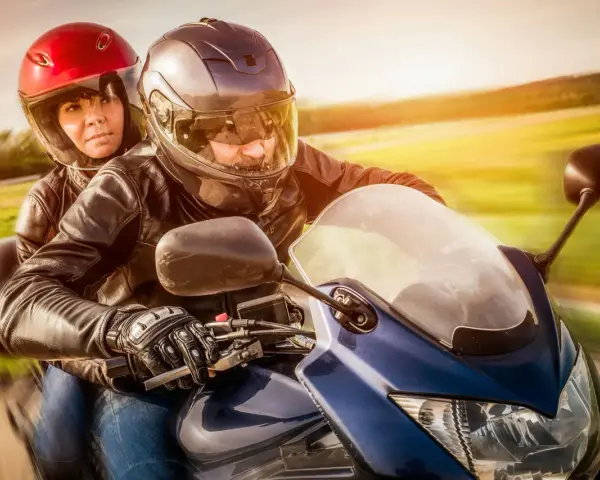 Coppia in moto, con lui alla guida e lei dietro, entrambi con caschi e giacche di pelle. Un'immagine che evoca la libertà di come guidare una moto.