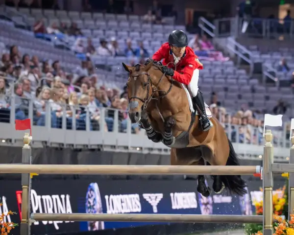 Cavalier en tenue rouge saute un obstacle lors d'une compétition équestre, visant la victoire à la **equestrian cup**.