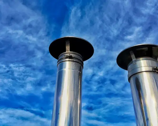 Due camini in acciaio inox, modello uni 7129 scarico a parete, brillano sotto un cielo blu con nuvole sottili.