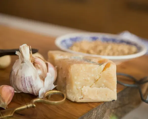 Kawałek parmezanu, czosnek i tarka na drewnianej desce.
