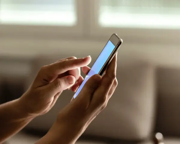 Dłonie trzymają smartfon, na ekranie którego wyświetla się niebieski kolor. Zastanawiasz się, jak sprawdzić ile lat ma telefon?