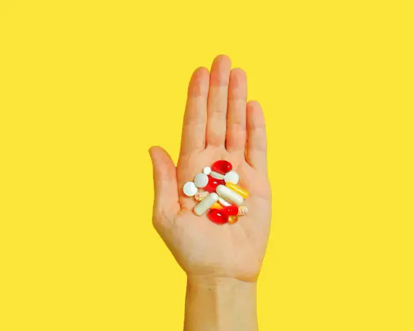 Hand hält bunte Pillen und Kapseln, die bei der Behandlung von Akne helfen könnten, wie z.B. Vitamin B5.