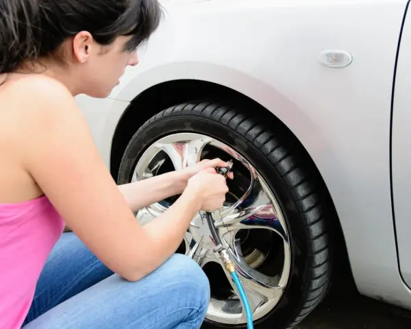 Donna in jeans e canotta rosa usa un compressore per gonfiare le gomme dell'auto, assicurandosi che siano alla pressione giusta.