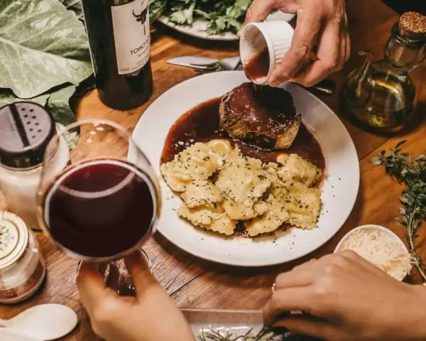Elegancka kolacja z ravioli i wołowiną w sosie. Idealne pytanie: jakie wino do gotowania? Czerwone wino i świeże zioła dopełniają atmosferę.