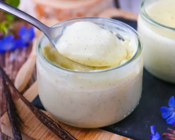 Délicieuse crème vanille recette, onctueuse et parsemée de grains de vanille, servie dans un pot en verre.