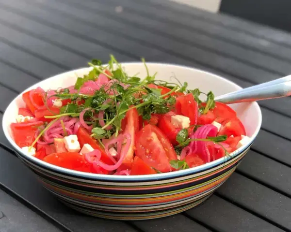 Enkel sallad med tomater, fetaost, rödlök och groddar i en färgglad skål.