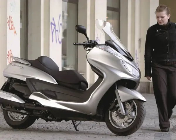 Srebrny skuter Yamaha Majesty 400, symbol miejskiej elegancji, obok kobiety w ciemnej kurtce.