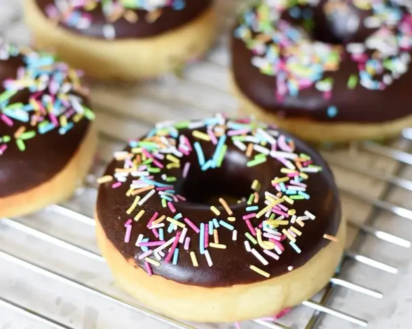 Färska, hembakade donuts med chokladglasyr och färgglatt strössel ligger på ett galler. Perfekt för att baka donuts!