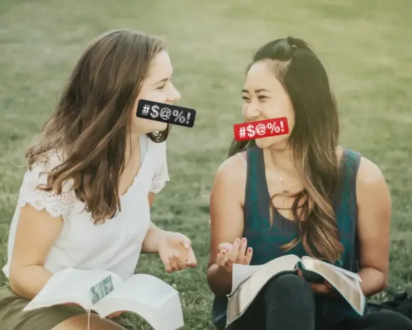 Two women with censored mouths discuss if cursing is a sin while reading books on the grass.