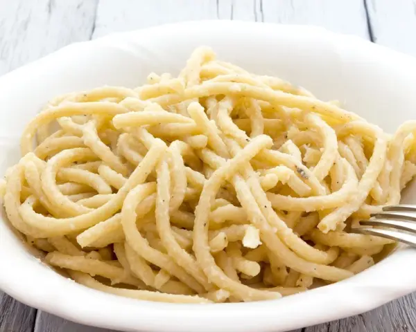 Pici, pasta fatta a mano con un'origine antica, servita in una ciotola bianca con una forchetta.