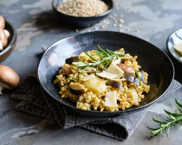 Miseczka risotto z grzybami i parmezanem, udekorowana rozmarynem.