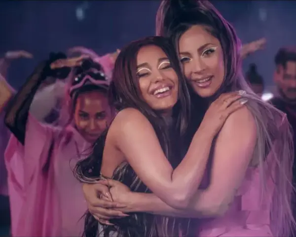 Ariana Grande i Lady Gaga przytulają się, otoczone tańczącymi ludźmi w różowych strojach. Czuć, że na nich "rain on me".