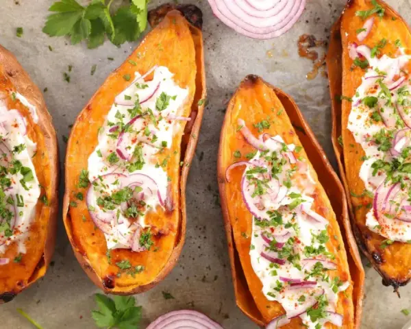 Quatre moitiés de patate douce au four, garnies de crème, oignons rouges et persil. Un délice simple et savoureux.