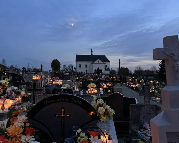 Cmentarz nocą, pełen płonących zniczy i kwiatów. W oddali kościół, a na niebie księżyc. Modlitwa świętej Gertrudy w ciszy zadumy.