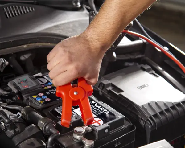 Starthilfe: Rote Klemme am Pluspol, warum nicht minus an minus? Ein Mann klemmt ein Starthilfekabel an die Autobatterie.