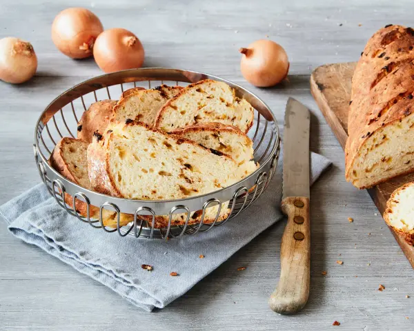 Frisch gebackenes Zwiebelbrot, bereit für ein leckeres Zwiebelbrot Rezept. Ganze Zwiebeln liegen daneben.