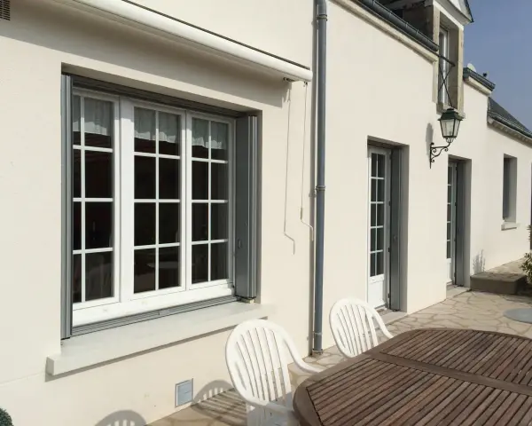 Un grand **appui de fenêtre** blanc orne la façade d'une maison. Des volets gris sont partiellement ouverts.