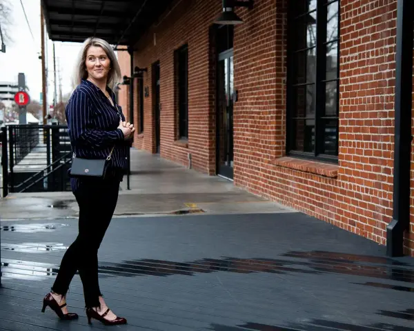 Mujer con outfit de camisa azul a rayas, pantalones negros y zapatos de tacón.