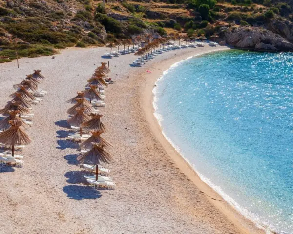 Rządki parasoli i leżaków na kamienistej plaży, obok krystalicznie czystej, turkusowej wody. To jedna z najpiękniejszych plaż w Europie.