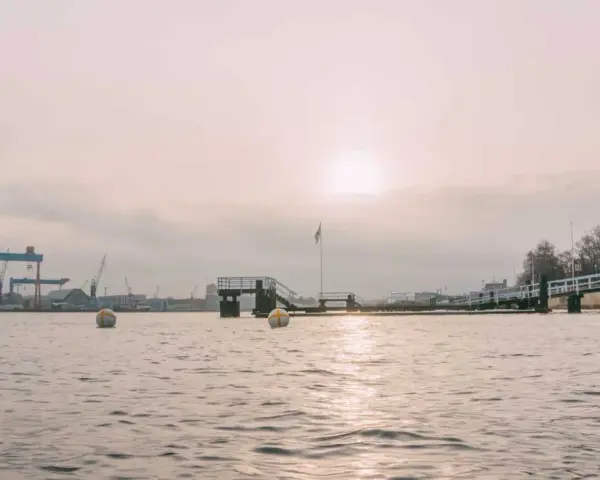 Kiel im Winter: Hafenkräne und eine Mole im nebligen Licht. Bojen treiben auf dem ruhigen Wasser.