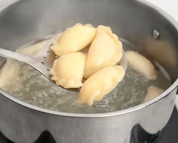 Pierogi gotujące się w garnku, wyjmowane łyżką cedzakową.