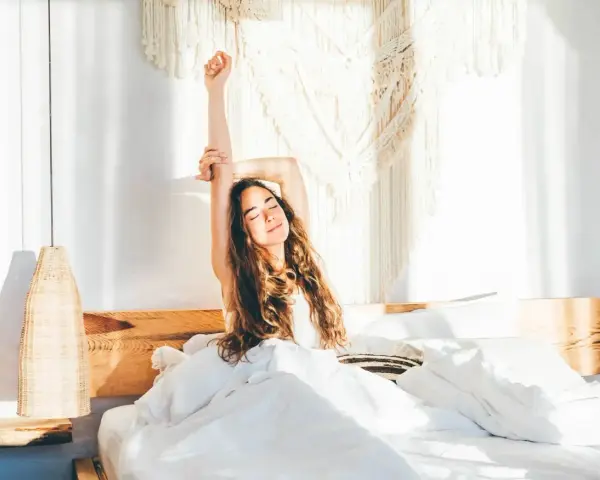 Eine Frau streckt sich im Bett aus, umgeben von weißer Bettwäsche. Sie genießt den Morgen, bereit, zusammen einzuschlafen und den Tag zu beginnen.