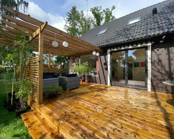 Trall med synliga skruvar kan vara en nackdel för utseendet. Här en altan med pergola, utemöbler och solrosor.