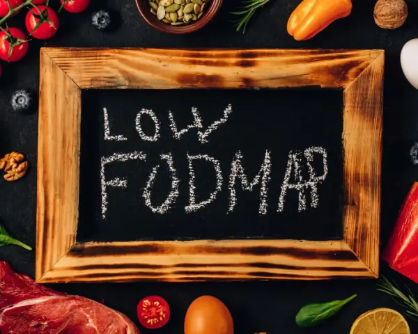 Na tablicy napis "LOW FODMAP". Wokół świeże produkty: mięso, ryba, pomidorki, cytryna, jajko, papryka, orzechy, jagody, szpinak.