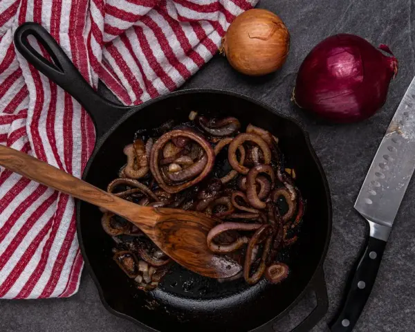 Cipolle in agrodolce caramellate in padella, pronte per essere gustate. Accanto, cipolle fresche e un coltello affilato.