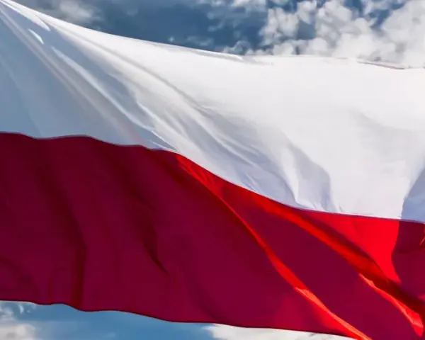 Flaga biało-czerwona powiewa na wietrze na tle błękitnego nieba z chmurami.