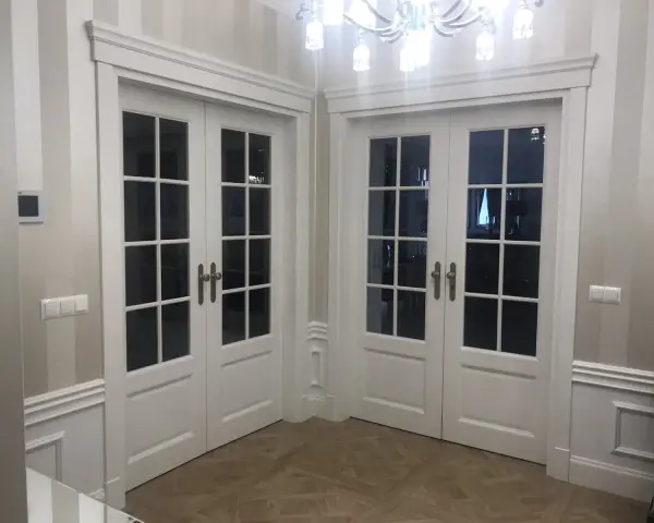 Eleganckie białe drzwi dwuskrzydłowe z przeszkleniem, osadzone w metalowych futrynach, tworzą stylowe przejście.