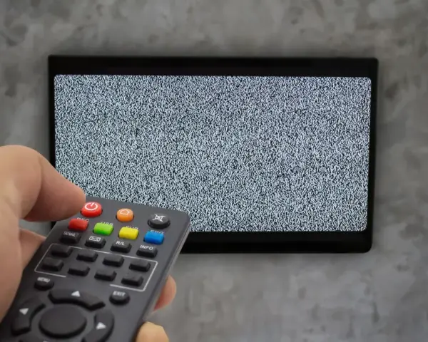 Ręka trzyma pilot dekodera, celując w ekran telewizora z zakłóceniami. Czas na naukę, jak sparować pilot dekodera z telewizorem.