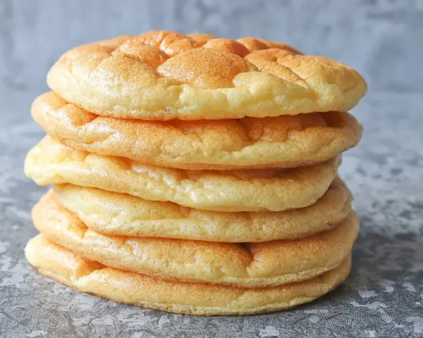 Una pila de pan nube, esponjosos y dorados, parecen nubes comestibles listas para ser disfrutadas.