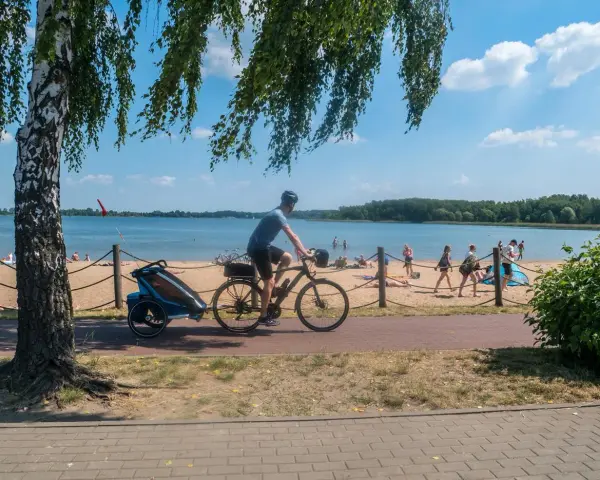 Mężczyzna na rowerze z przyczepką jedzie ścieżką rowerową wzdłuż plaży. To idealne miejsce na wycieczkę trasą pogoria 3.