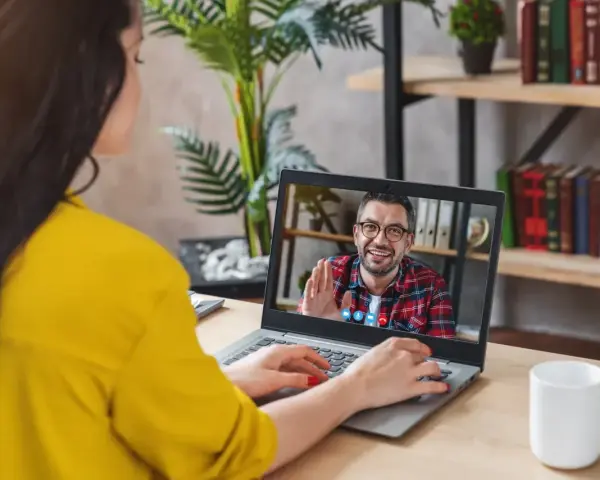 Kobieta na wideo rozmowie z mężczyzną, który uśmiecha się i macha. Może to być konsultacja online, np. test na autyzm.