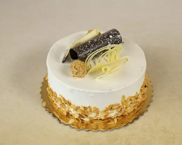 Elegancki tort rafaello z wiórkami migdałowymi, czekoladową rurką i dekoracjami z białej czekolady.